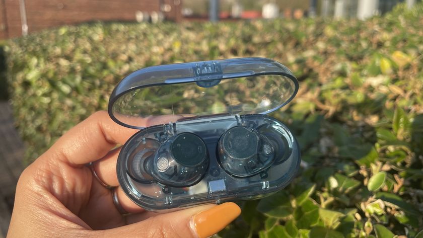 A pair of blue transparent Sony WF-C710N earbuds in their charging case held in front of a hedge.