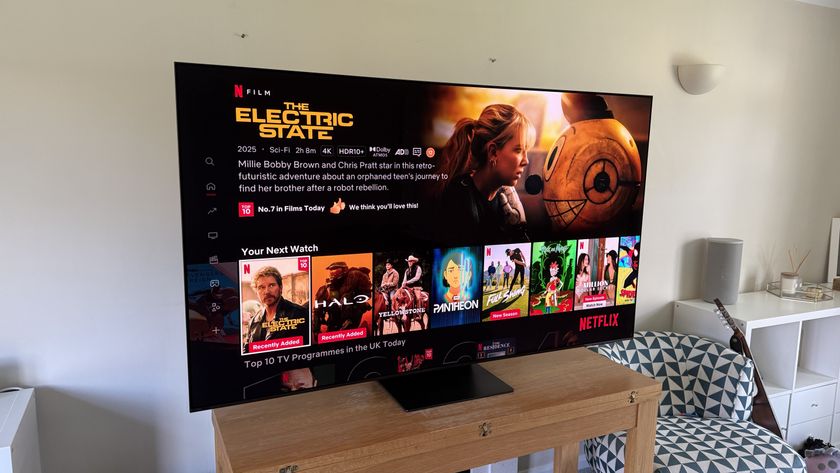 The 65-inch Samsung S95C OLED TV photographed on a wooden table in a living room. On the display is the Netflix homescreen.